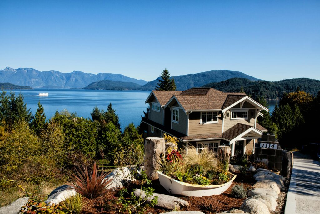 Scenic view of a charming house by the lake surrounded by mountains and lush greenery.